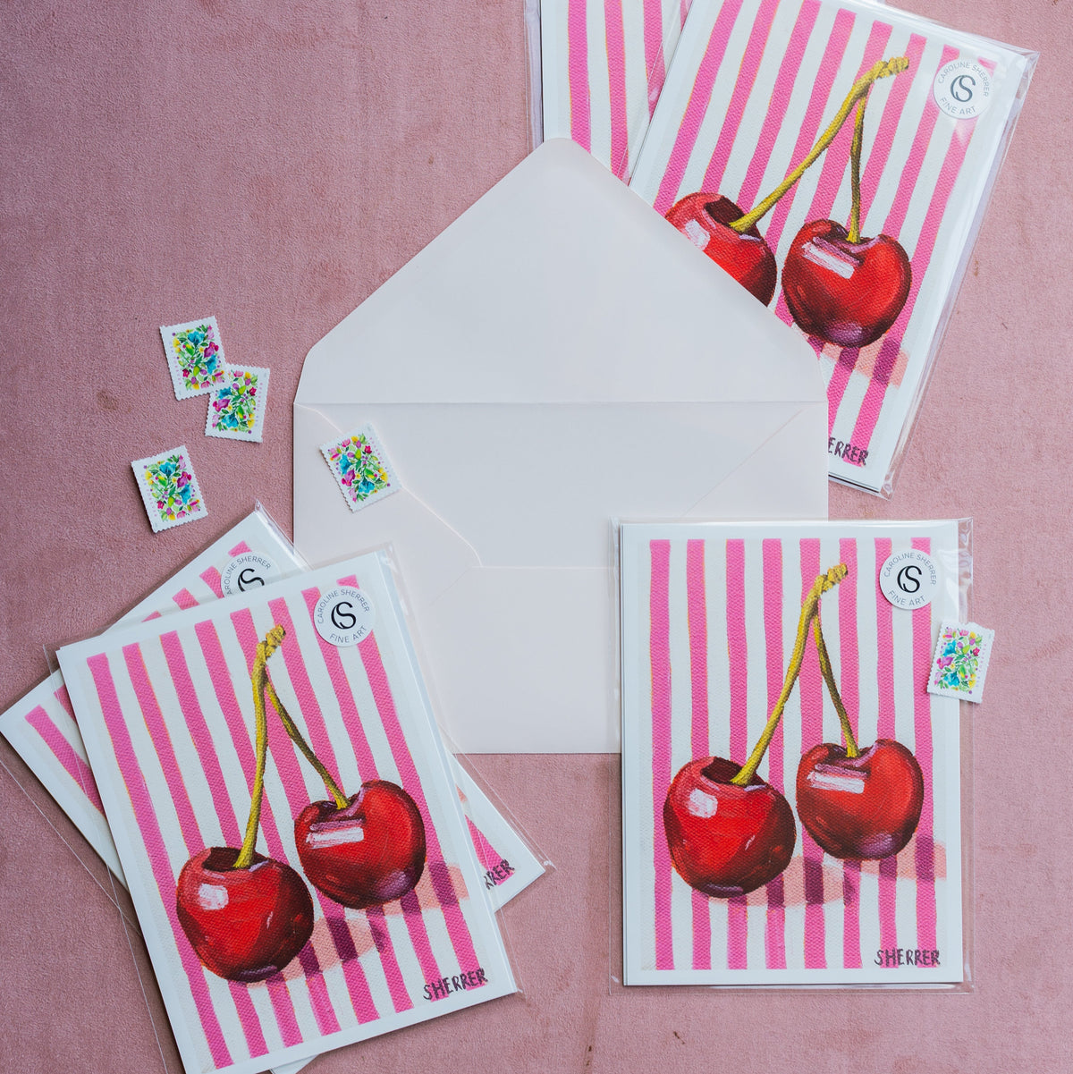 Example Print Club cherry prints in clear sleeves beside a stamped white envelope on a pink surface.