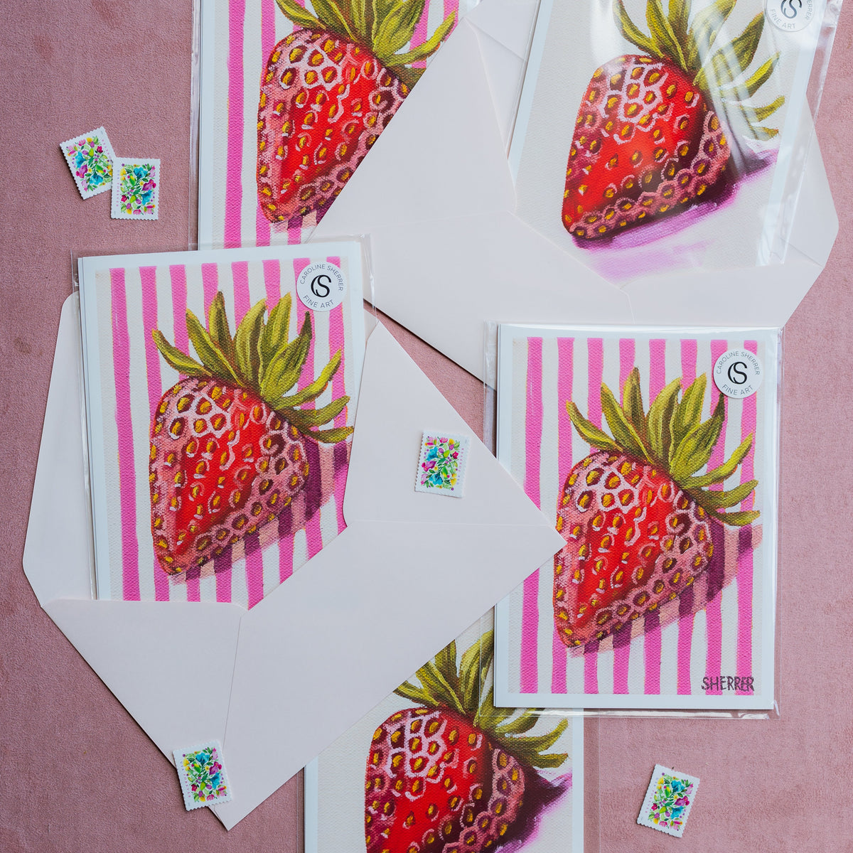 Example single-strawberry art prints in clear sleeves with white envelopes and floral postage stamps.