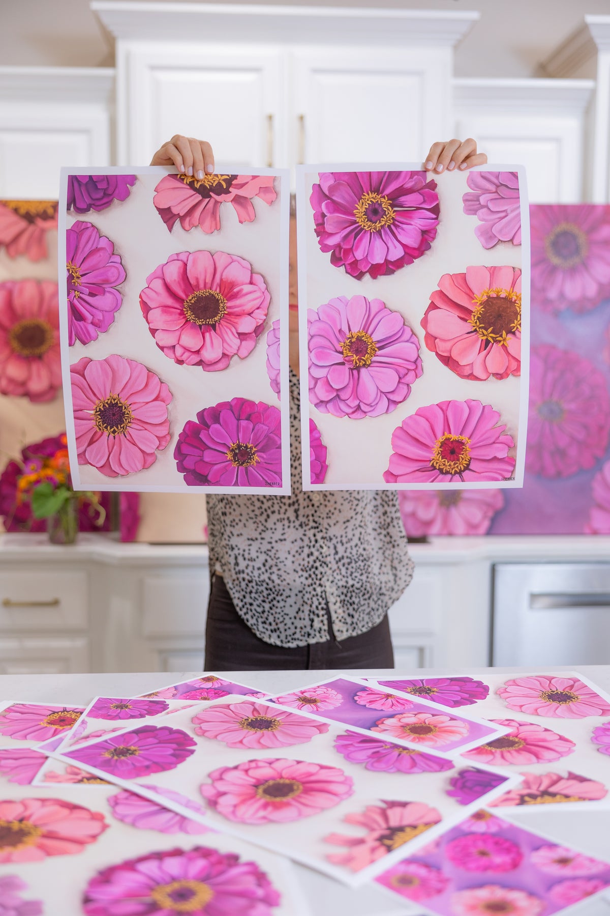 Caroline Sherrer holding two white-bordered Garden Party floral prints side by side, with more prints spread across the table.