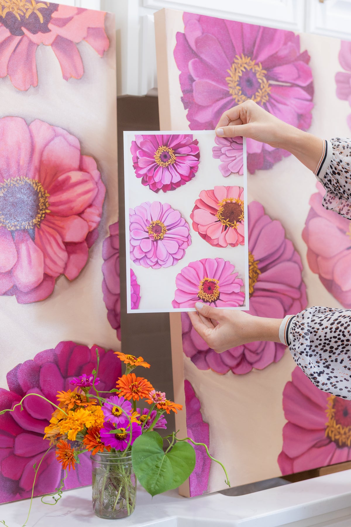 Hands holding a white-bordered Garden Party II print in front of its matching painting, with fresh flowers below.
