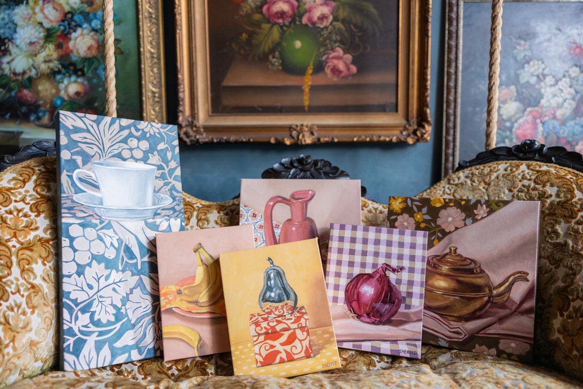 Colorful still-life paintings displayed together on an ornate upholstered settee.