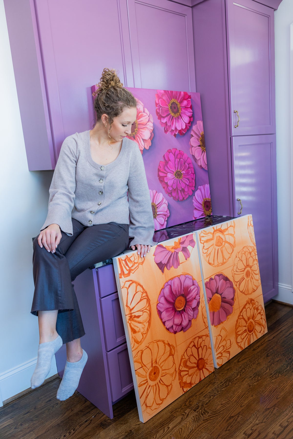 Caroline Sherrer seated among colorful floral paintings in her studio.