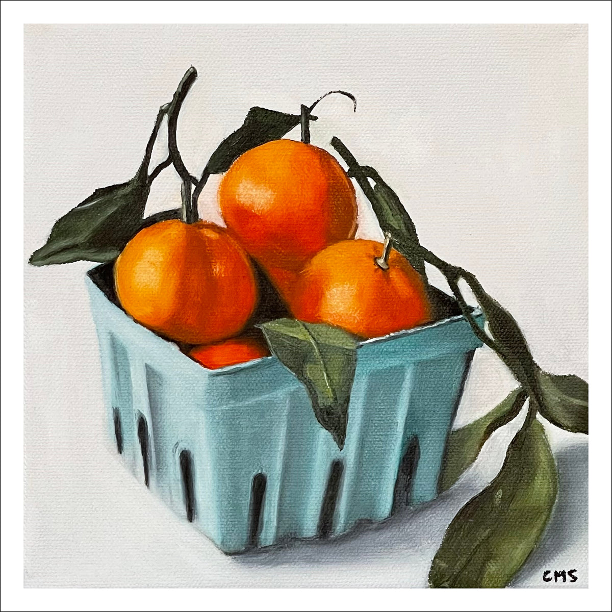Oranges Blue Basket fine art print by Caroline Sherrer, featuring oranges with leafy stems resting in a teal blue cardboard basket.