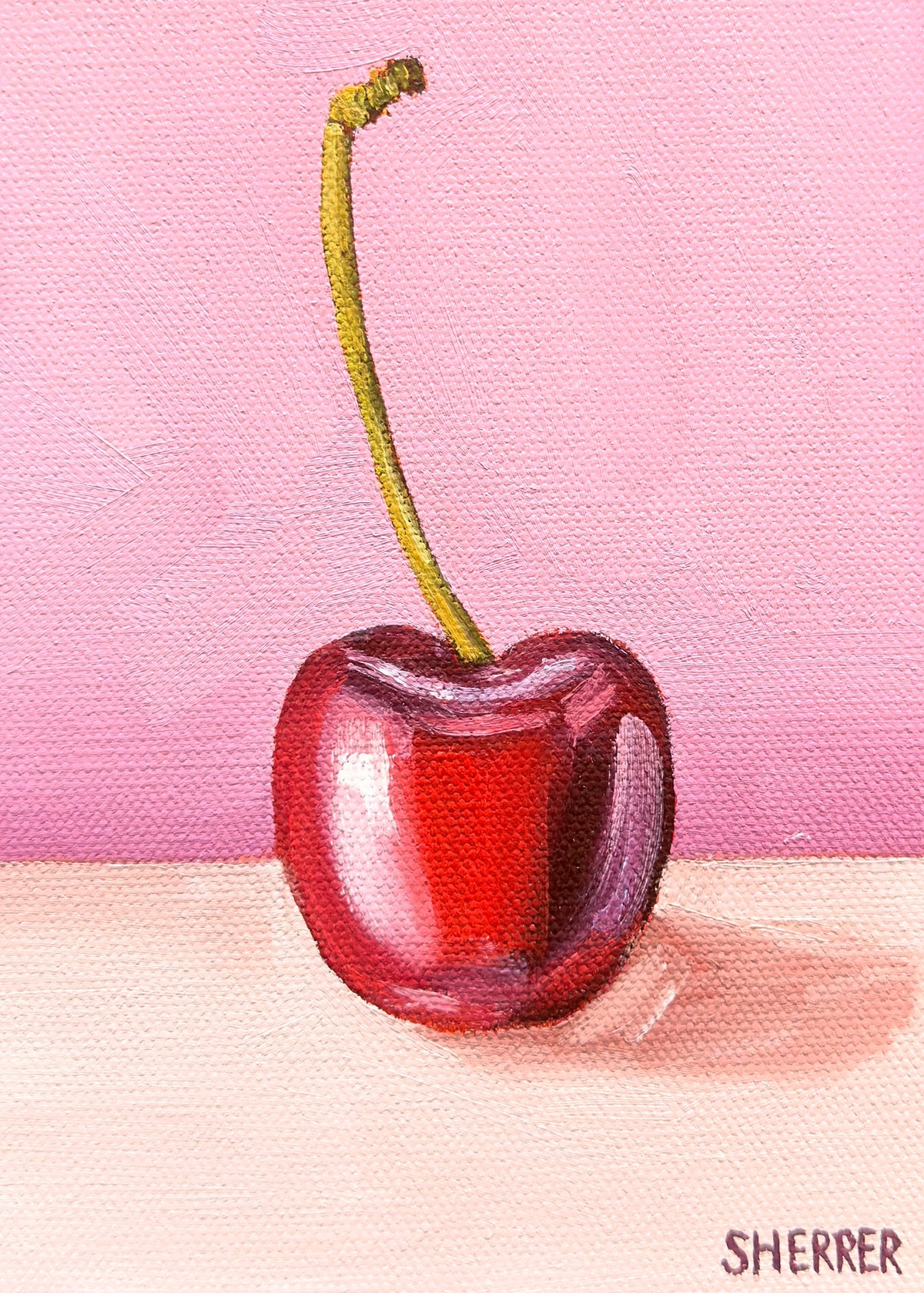 Cherry Blush, original oil painting by Caroline Sherrer, featuring a cherry resting on a background where the upper two thirds is blush pink and the bottom one third is a light tanish white.