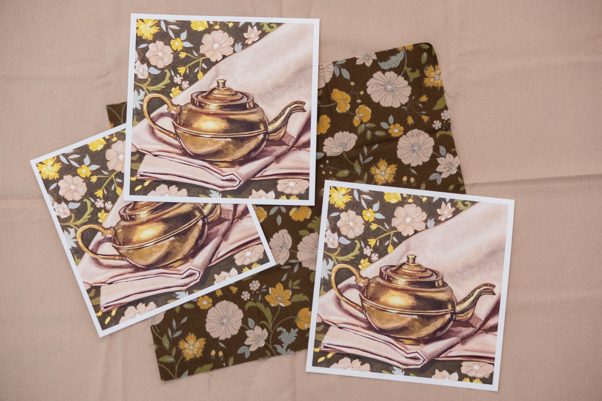 Three white-bordered Kettle on Florals prints arranged over brown floral fabric on a blush surface.