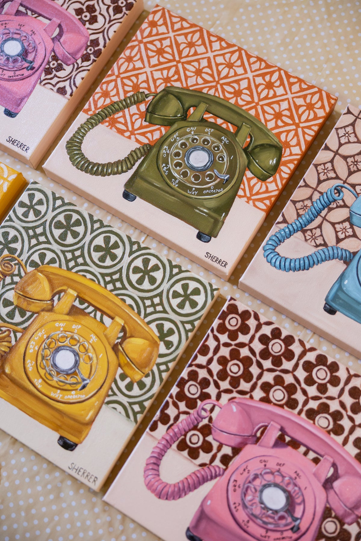 Angled arrangement of green, yellow, blue and pink rotary-telephone paintings with contrasting patterned backgrounds.