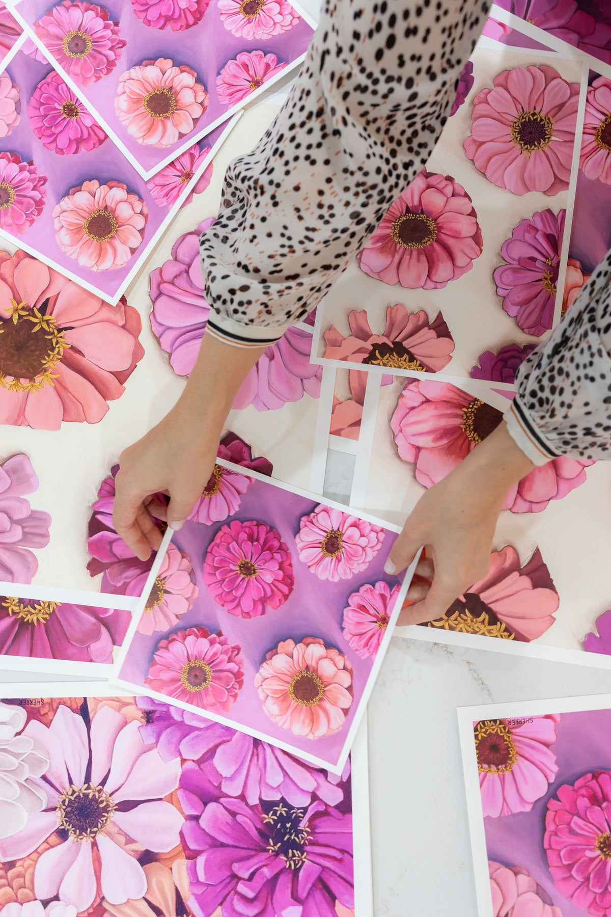 Overhead view of hands arranging a white-bordered Bold Blooms print among other pink and purple floral prints.