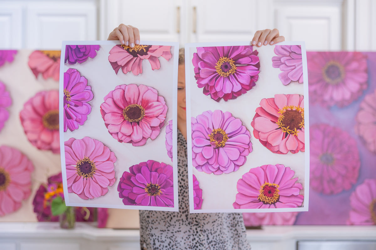 Two white-bordered Garden Party floral prints held side by side in front of the original pink-and-purple flower paintings.