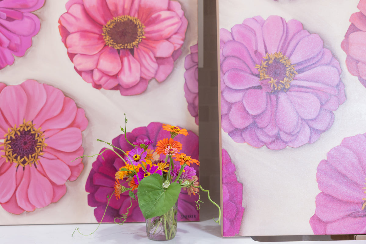 Garden Party floral paintings with large pink and purple zinnias displayed behind a small vase of fresh flowers.