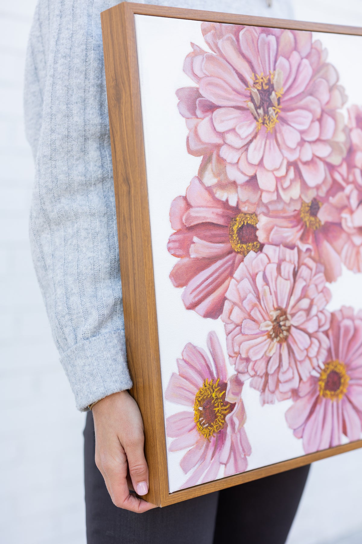 Angled close-up of Spring Zinnias held at the artist's side, showing pink petals and its wooden frame.