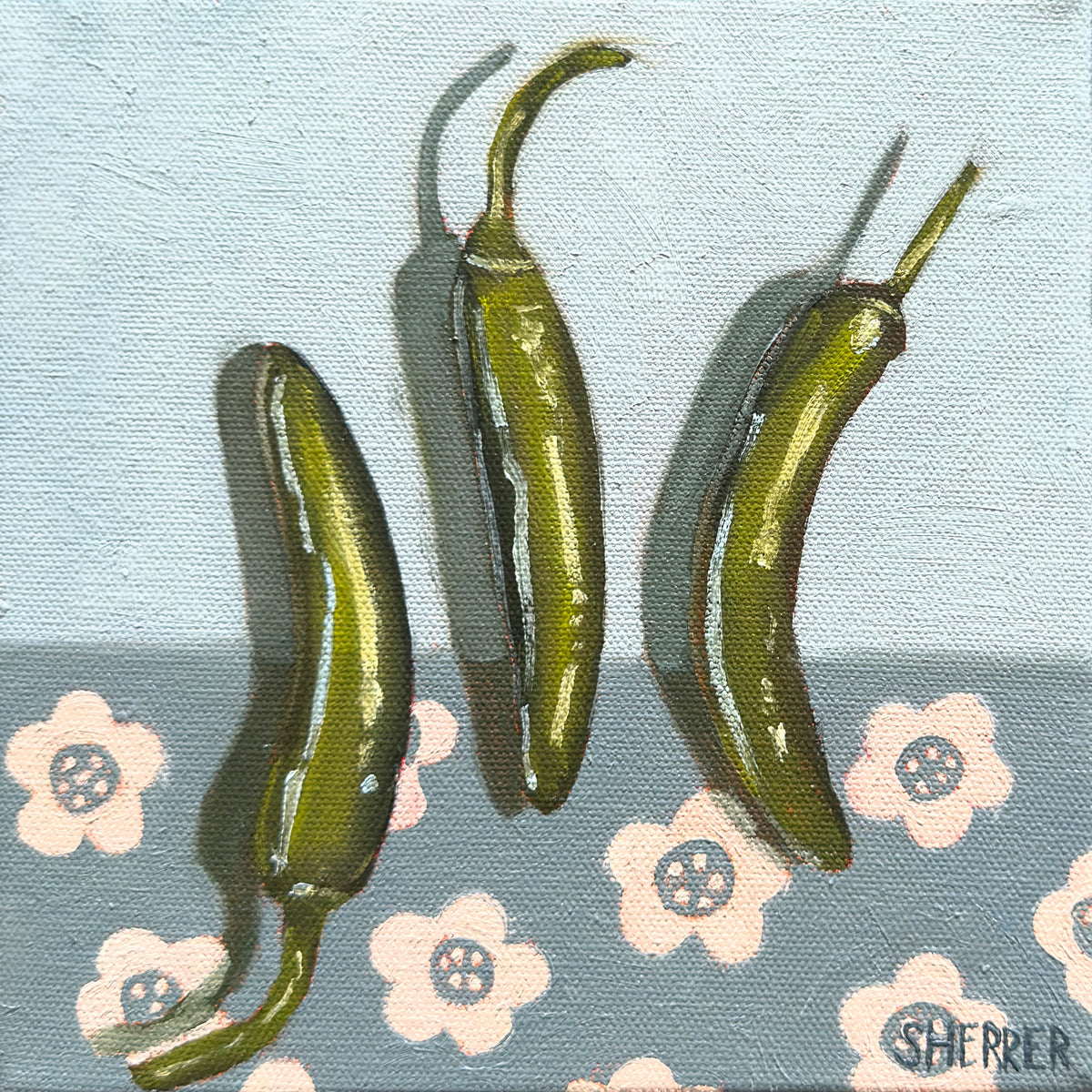 Three Amigos on Florals, original oil painting by Caroline Sherrer, featuring three green narrow peppers resting on a light blue background. The bottom half of the background is a darker blue featuring a cream colored floral pattern.